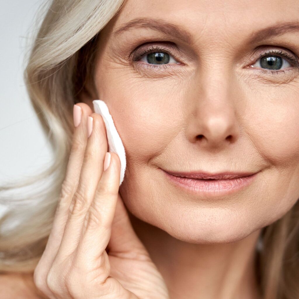 Woman smiling at camera and wiping her face with a cotton pad