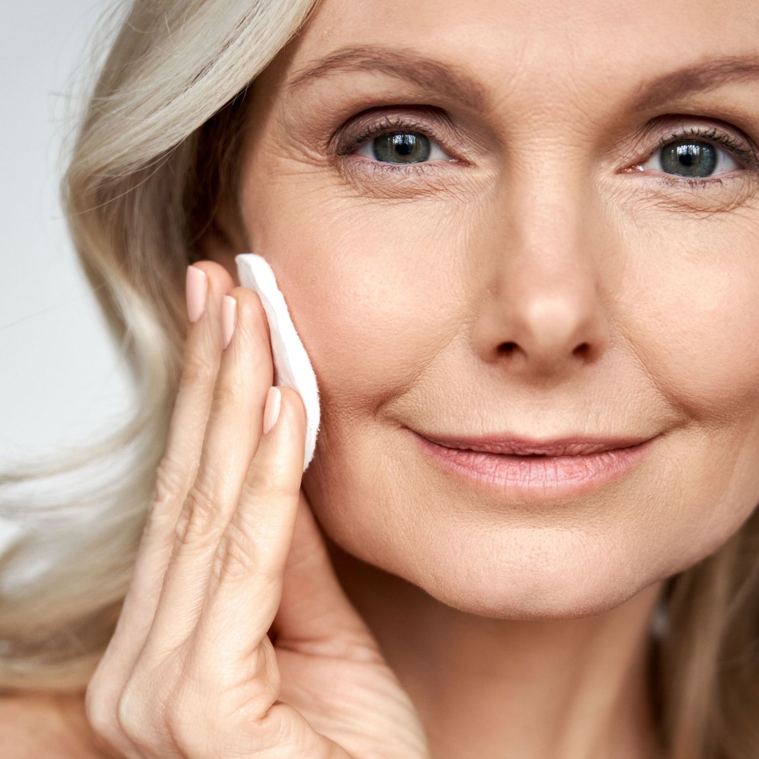 Woman smiling at camera and wiping her face with a cotton pad